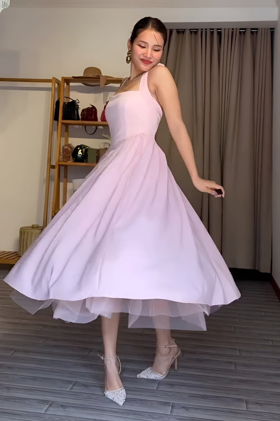 Woman in a pink dress holding a red rose in a room with a chandelier and shelves.