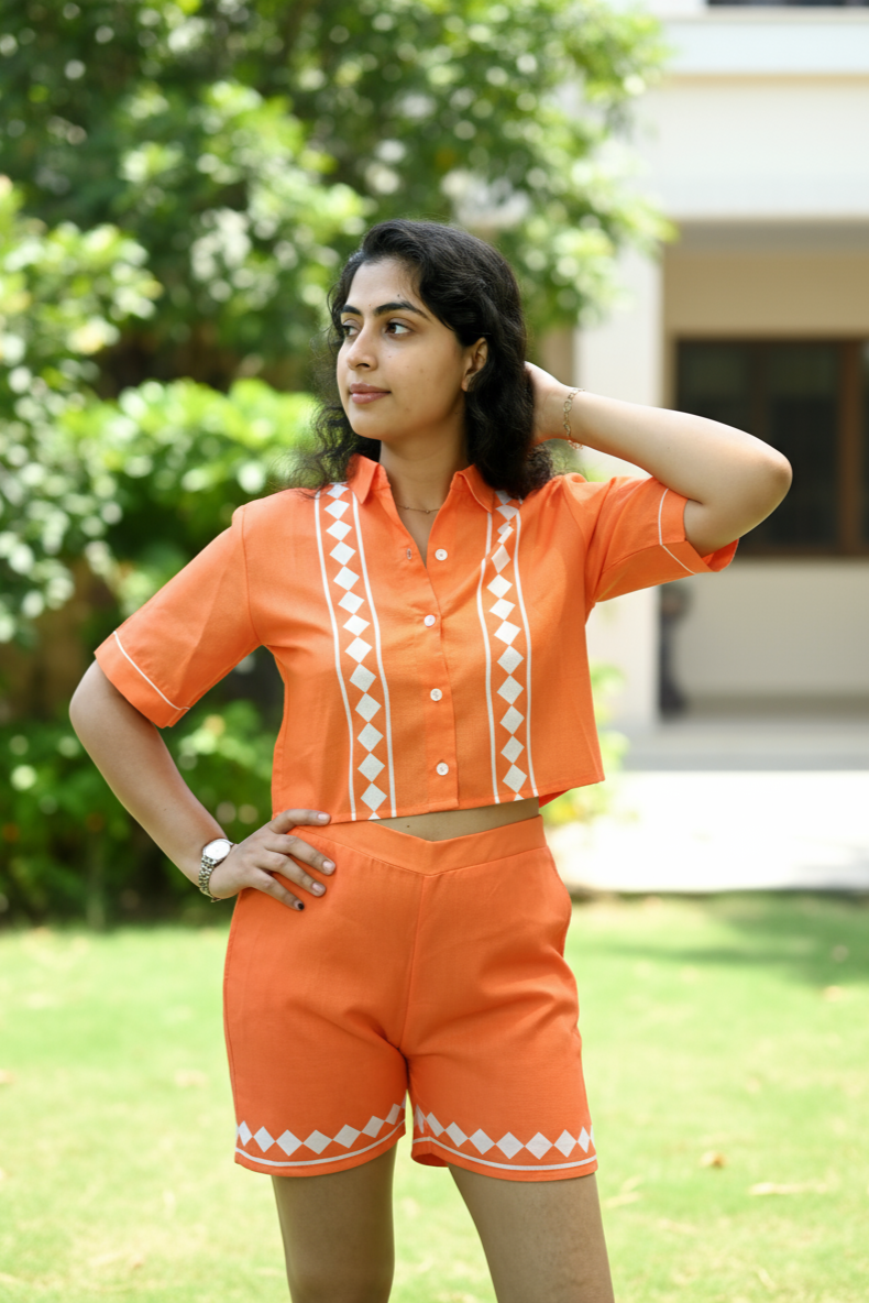 Woman in an orange outfit with white patterns standing outdoors.