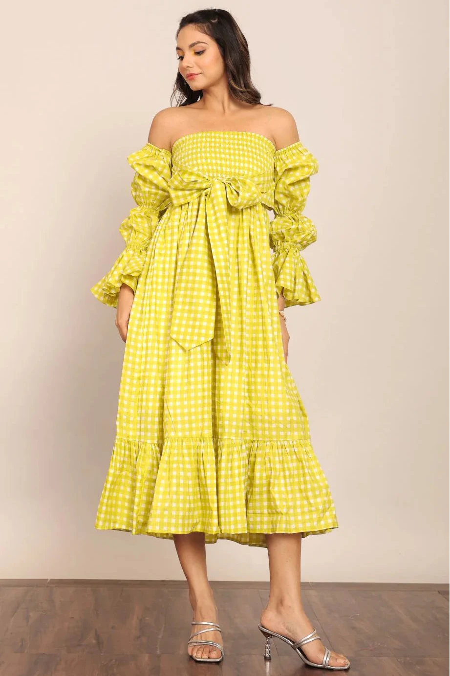 Woman wearing a yellow checkered dress with ruffled sleeves against a beige background