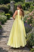 Woman in a yellow dress walking through a garden with flowers and a building in the background