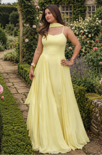 Woman in a yellow dress standing in a garden with a historic building in the background