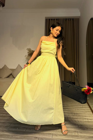 Woman in a yellow dress standing in a room with a couch and decorative pillows.