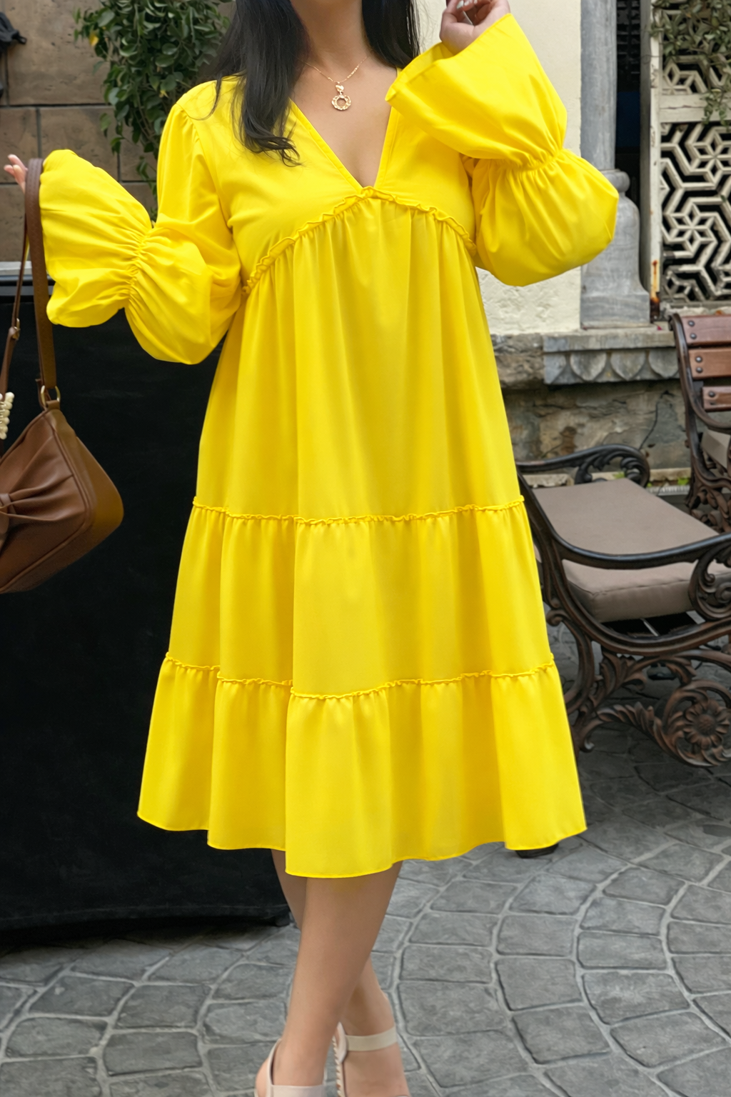 Woman wearing a yellow dress with long sleeves in an outdoor setting.